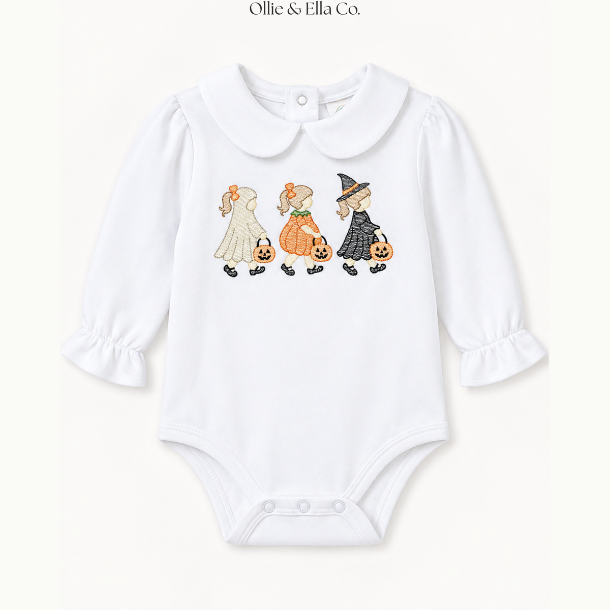 A white long-sleeve baby bodysuit with a Peter Pan collar, featuring a printed graphic of three children dressed in Halloween costumes walking with pumpkins. The brand name 'Ollie & Ella Co.