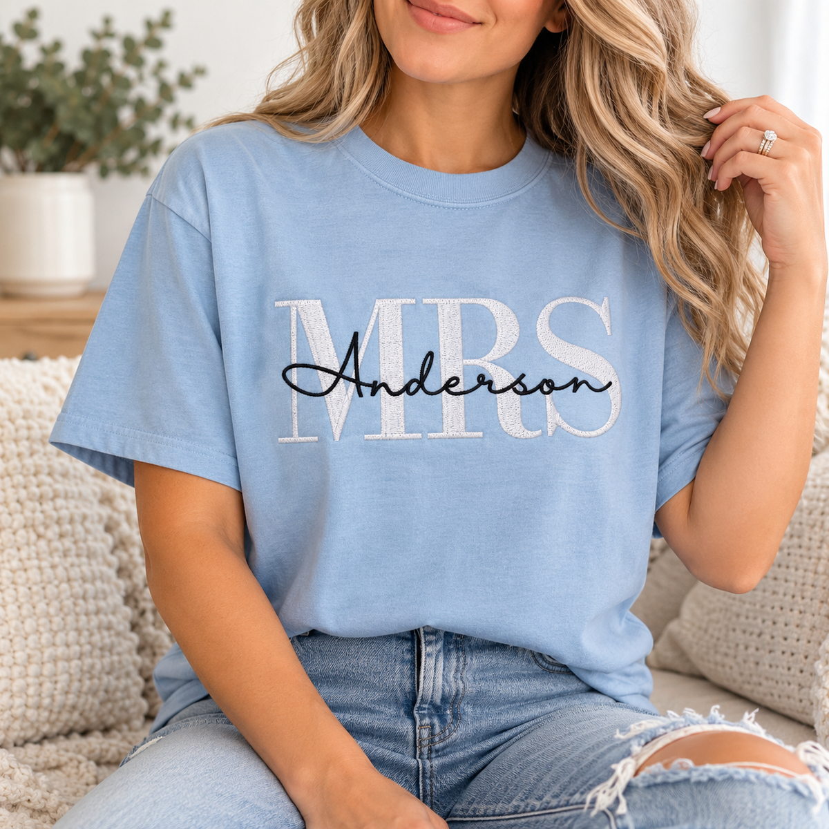 A woman wearing a light blue graphic t-shirt with 'MRS Anderson' printed on the front, sitting on a cozy knit couch.